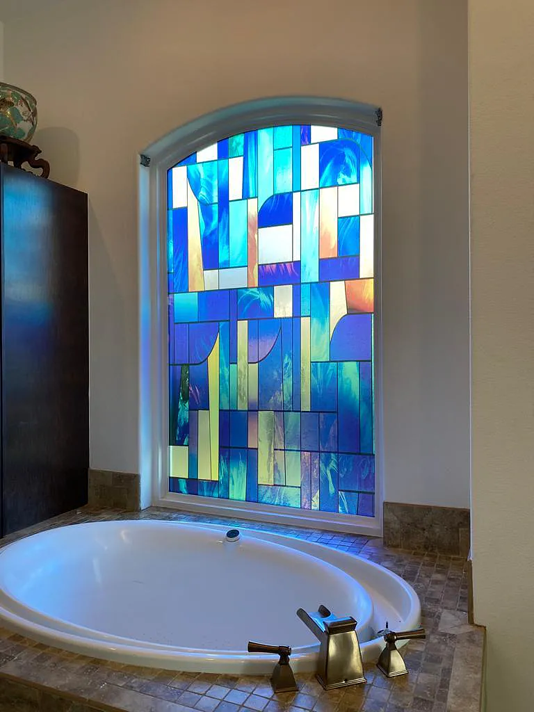 Arched bathroom window above soaking tub with SXEG-1027MTSF Abstract Stained Glass film in vivid blues
